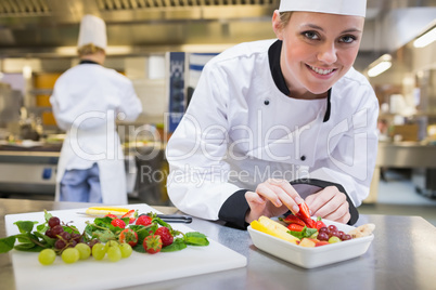 Smiling chef putting a strawberry in the fruit bowl