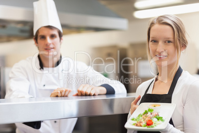 Waitress holding salmon dish smiling with chef