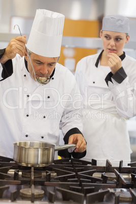 Teacher tasting his students soup with her watching anxiously