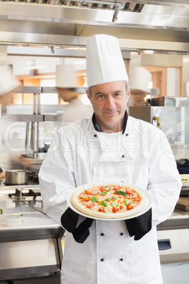 Chef showing pizza in busy kitchen