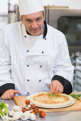 Happy chef giving finishing touch to pizza