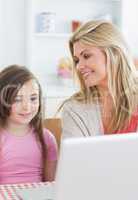 Mother smiling at daughter using laptop