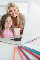 Mother standing behind daughter looking at laptop
