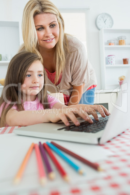 Woman standing looking at Daughter typing