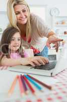 Mother pointing at laptop with daughter sitting down