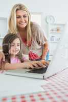 Little girl typing with mother watching at laptop