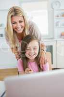 Little girl pointing at laptop and laughing with mother