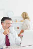 Man drinking coffee while checking laptop