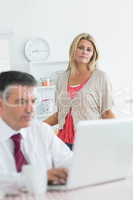 Wife looking upset at husband using laptop in kitchen