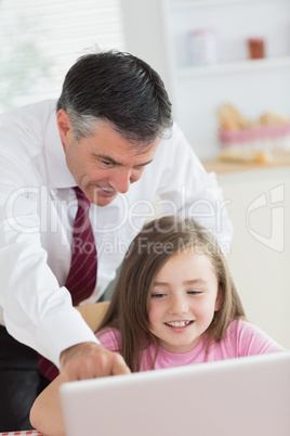 Father pointing at something on daughter's laptop and smiling