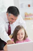 Father pointing at something on daughter's laptop and smiling