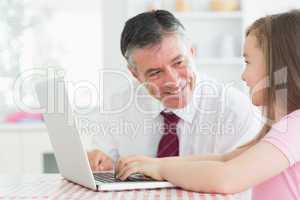 Man and daughter sitting at the kitchen at laptop