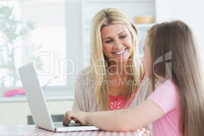 Woman and daughter sitting at the kitchen at laptop