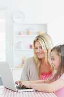 Woman and little girl sitting at the kitchen with laptop
