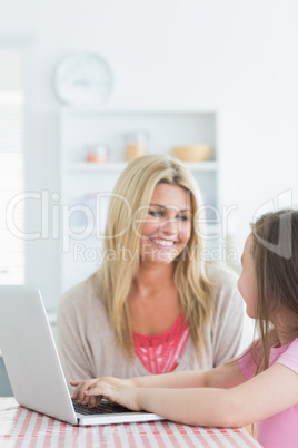Woman and daughter sitting at the kitchen smiling with a laptop
