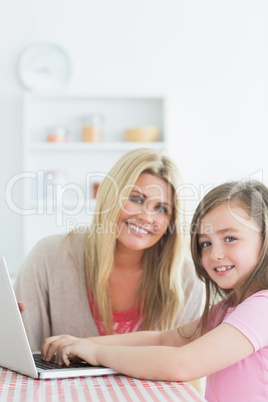 Woman and daughter sitting at the kitchen while smiling with a l