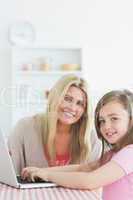 Woman and daughter sitting at the kitchen while smiling with a l