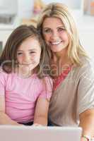 Woman and daughter sitting smiling with laptop