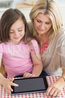 Child using tablet pc with mother in kitchen