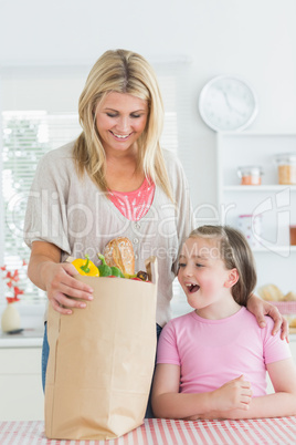 Woman looking into grocery bag beside smiling daughter