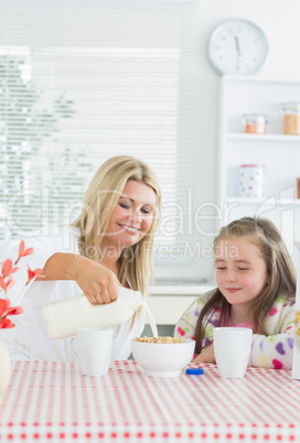 Mother pouring milk into cereal bowl for daughter