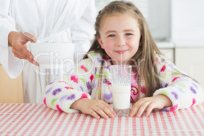 Happy little girl with glass of milk getting cereal from her mot