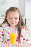 Little girl sitting while smiling with glass of orange juice