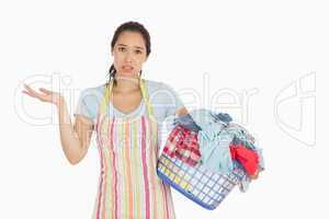 Puzzled young woman holding laundry basket full of dirty laundry