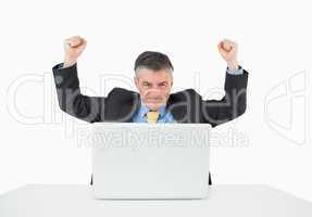 Cheering man sitting at his desk with laptop