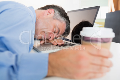 Man sleeping on his laptop while holding coffee