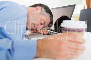 Man sleeping on his laptop while holding coffee