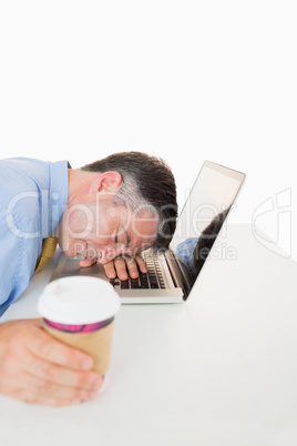 Tired man sleeping on his laptop while holding coffee