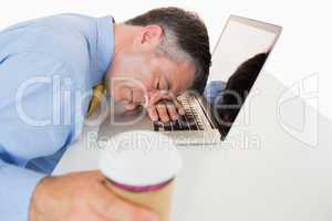 Exhausted man sleeping on his laptop while holding coffee