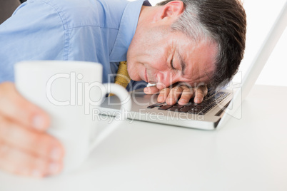 Man sleeping on his laptop while holding coffee