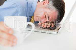 Man sleeping on his laptop while holding coffee