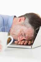 Overworked man sleeping on his laptop while holding coffee