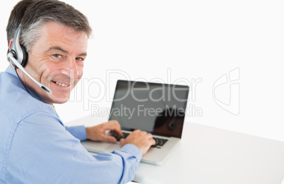 Smiling businessman with headset working on laptop Smiling businessman with headset working on laptop