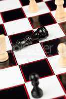 Black queen lying at the chessboard while white standing