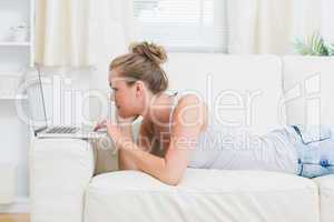 Woman typing on the laptop while lying on the sofa