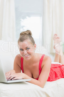 Woman smiling while relaxing on the sofa with laptop