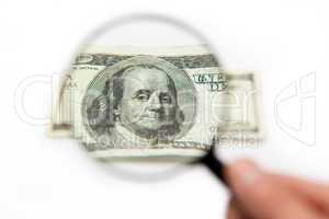 Hand holding magnifying glass over dollar bill