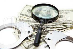 Handcuffs dollars and a magnifying glass