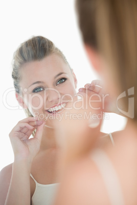 Cute woman using dental floss in front of mirror