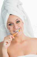 Smiling woman with hair towel washing her teeth
