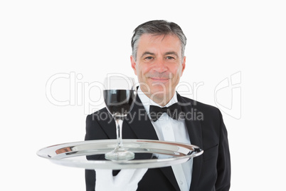 Smiling waiter holding a glass of wine on a silver tray