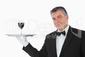 Smiling waiter holding a glass of wine on a silver tray