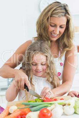 Mother teaching her daughter cutting vegetables