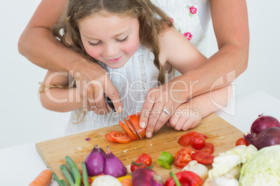Mother helping her daughter to cut tomato