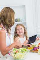 Mother cutting vegetables with her daughter using tablet
