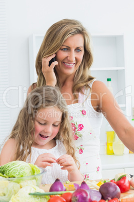 Mother phoning while her daughter working with vegetable